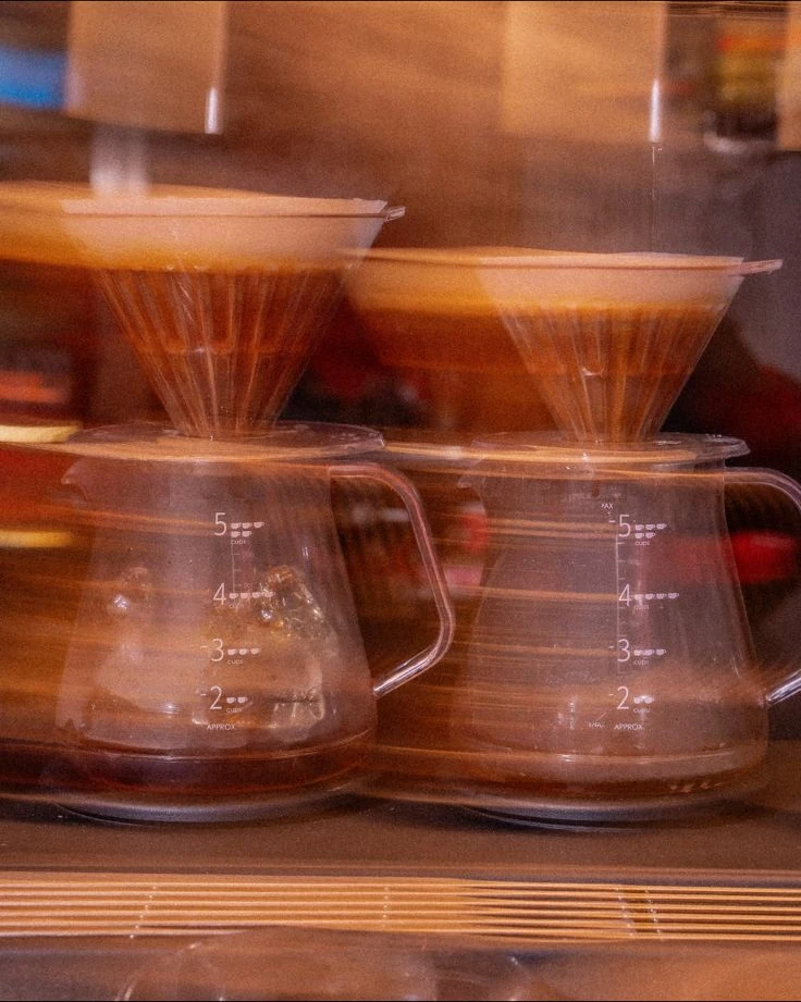 مصفاتا V60 تقطّران القهوة في إبريقين زجاجيين على بار ايت، مصوّرة بتعريض طويل
