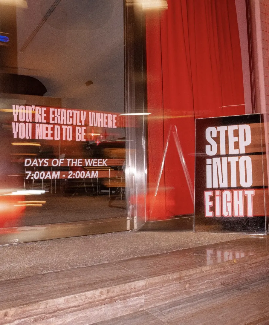 واجهة ايت الزجاجية ومكتوب عليها YOU'RE EXACTLY WHERE YOU NEED TO BE وأوقات الدوام، وبجانبها لوحة STEP INTO EiGHT